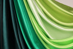 a close-up view of a collection of colorful satin fabric, with a gradient of green and black hues. The fabric appears to be folded or draped, creating a visually striking and textured composition.