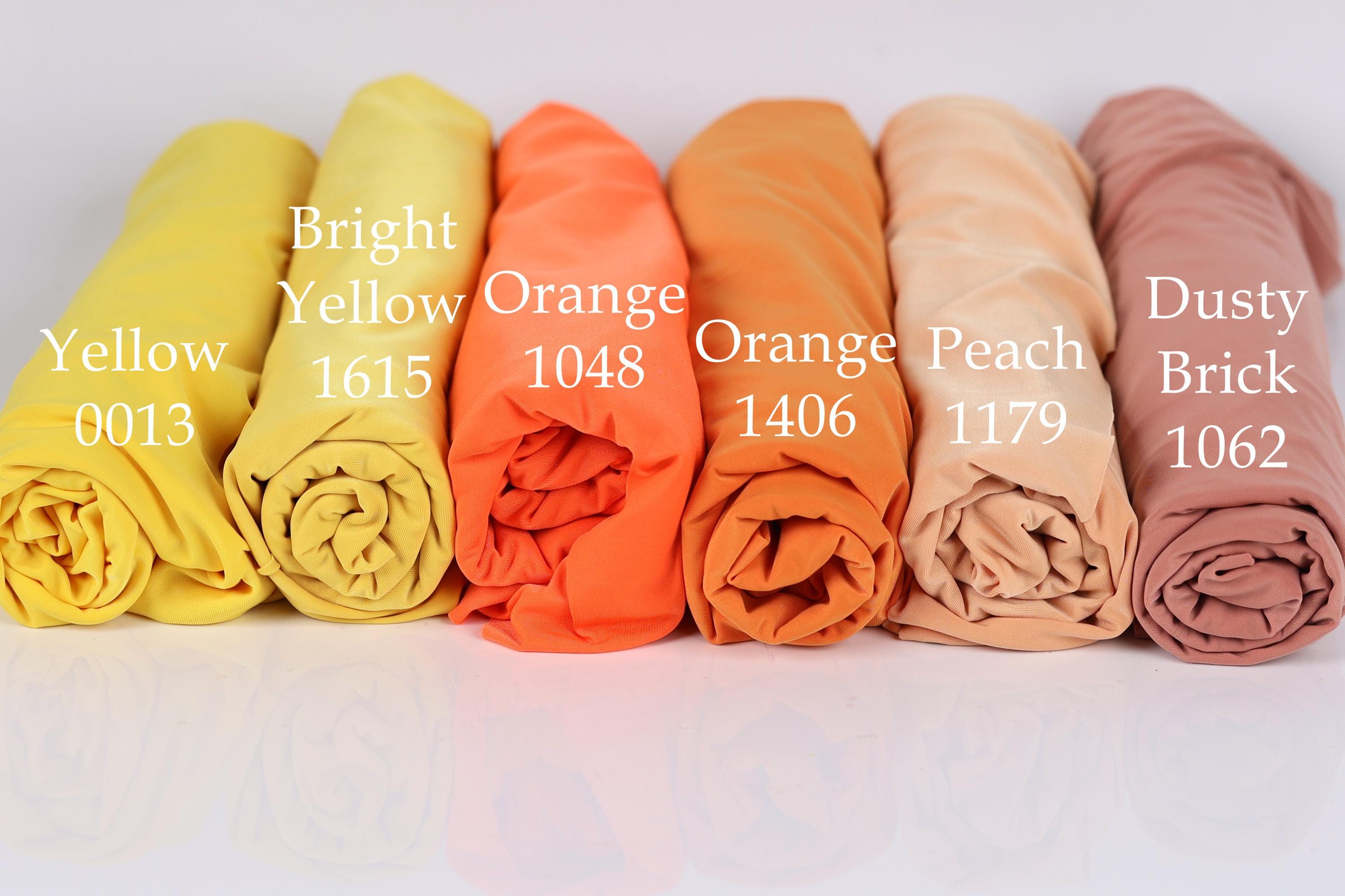 six rolled-up fabric swatches in different colors, including bright yellow, orange, peach, dusty brick, and peach.