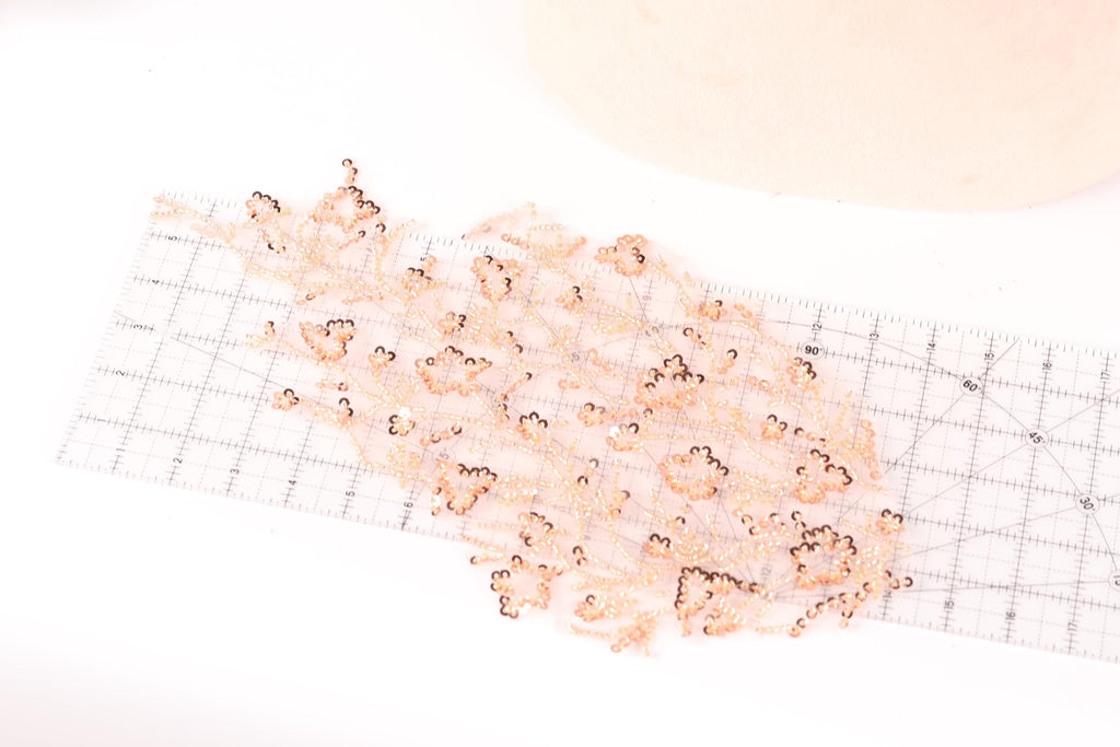 a collection of small, delicate, and intricate beaded or sequined objects arranged on a transparent ruler, which is placed on a white surface.