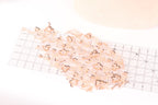 a collection of small, delicate, and intricate beaded or sequined objects arranged on a transparent ruler, which is placed on a white surface.