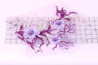 a close-up view of a delicate floral arrangement composed of purple and white flowers, with some purple flowers and leaves. The arrangement is placed on a transparent surface, allowing the viewer to see the intricate details of the flowers and leaves.