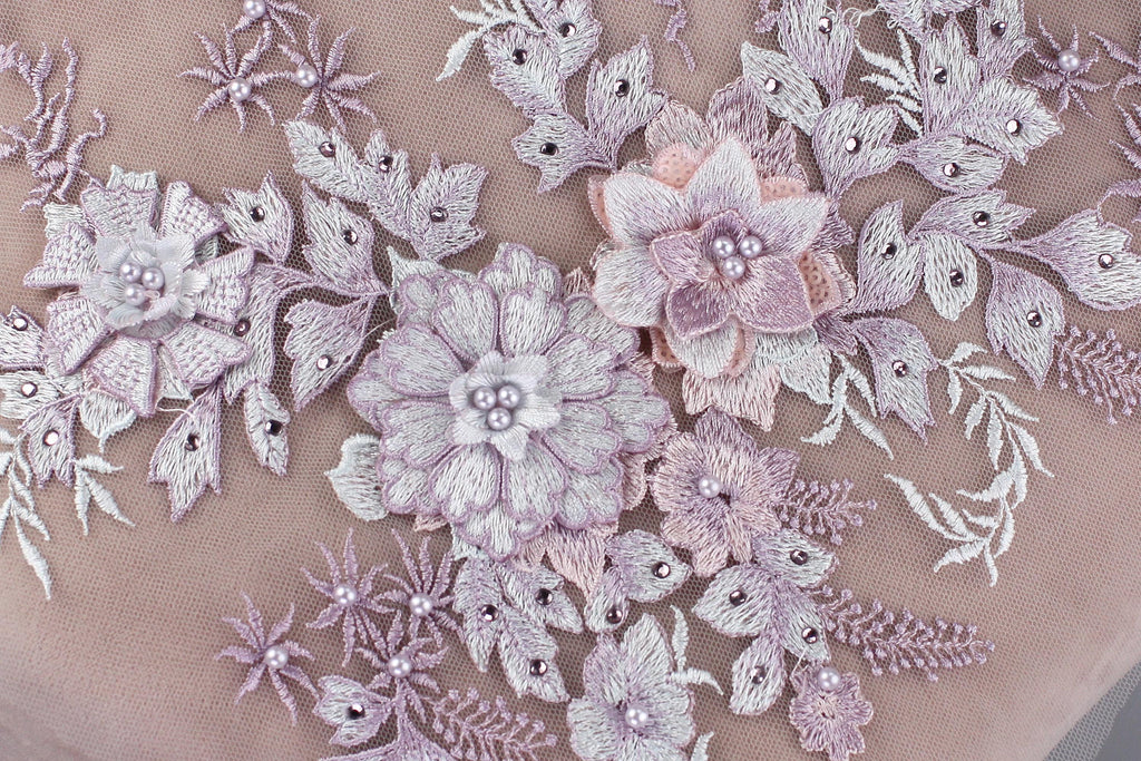 a close-up view of a delicate, intricate embroidered design with a variety of flowers and leaves in shades of pink and white.