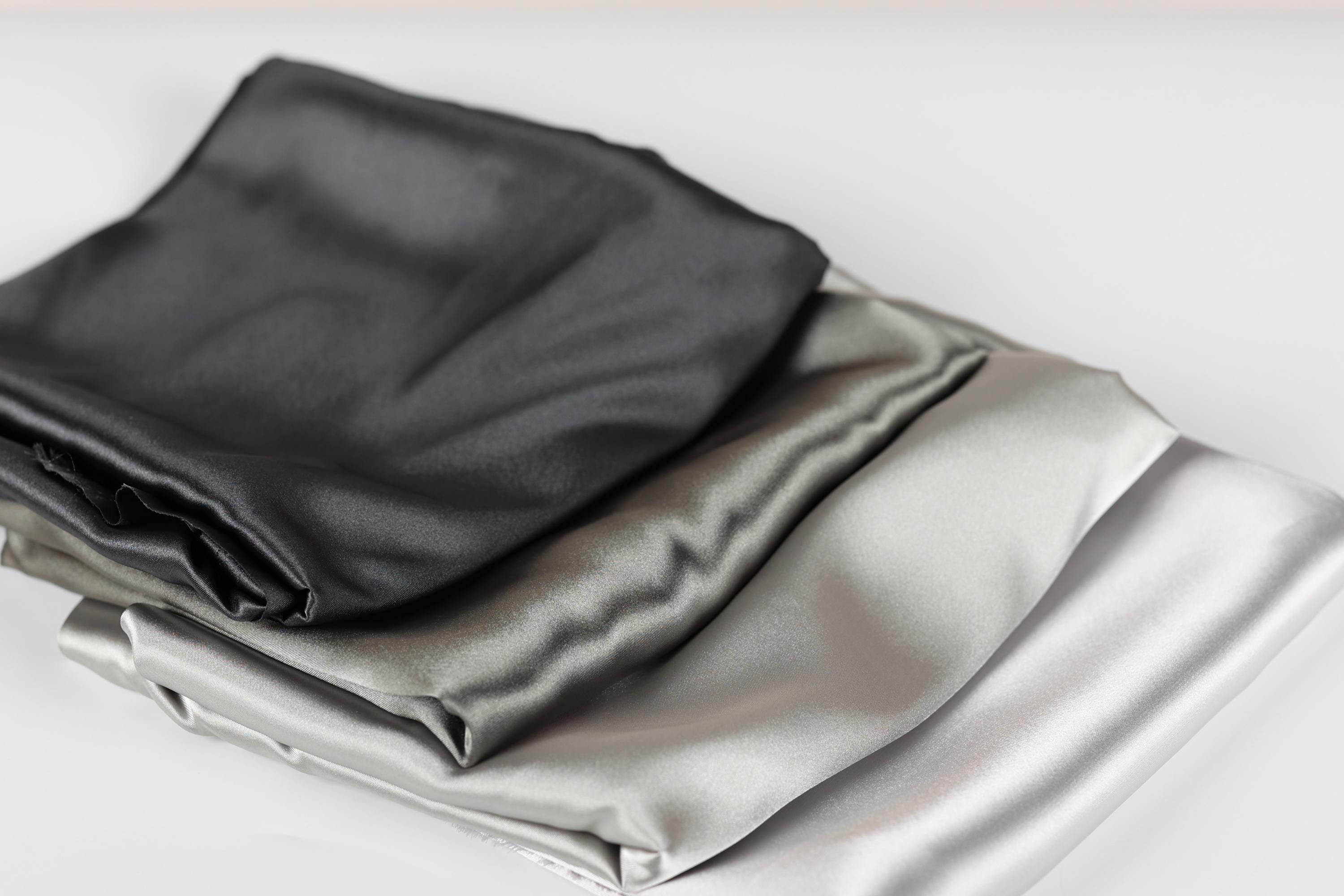 a close-up view of three folded satin fabric pieces in different colors: black, gray, and white.