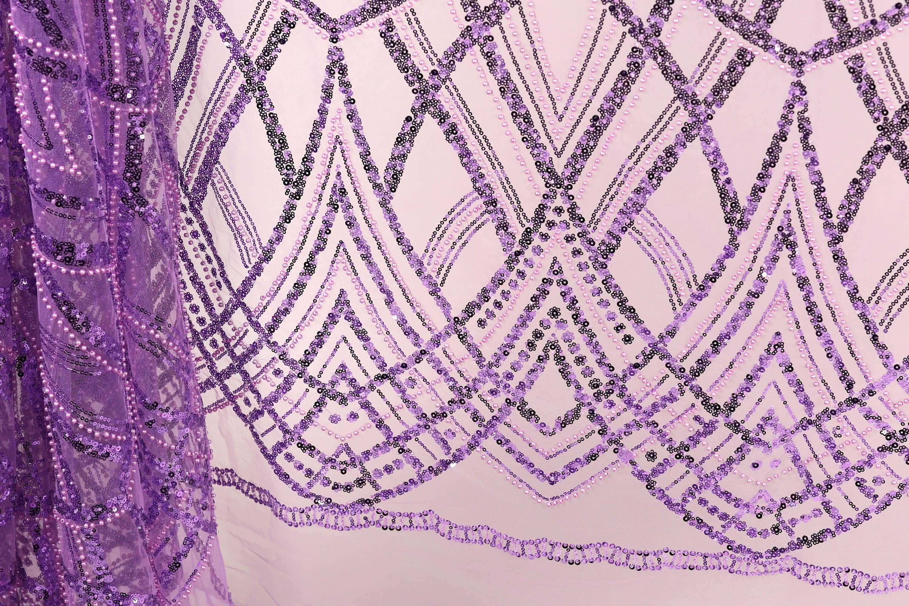a close-up view of a fabric with a purple and black sequin pattern. The fabric appears to be a sheer material, with a repeating pattern of diamond shapes and lines in shades of purple and black. The pattern is intricate and visually striking, with the sequins adding a touch of sparkle and texture to the overall design.