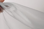A hand is holding a piece of white fabric, which appears to be a sheer material. The fabric is being held up against a plain white background, creating a simple and minimalist visual composition.