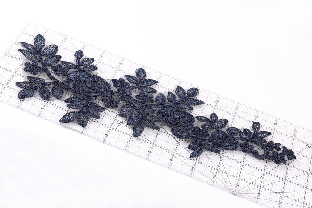 a close-up view of a piece of fabric with a floral pattern, including leaves and flowers, placed on a ruler for scale.