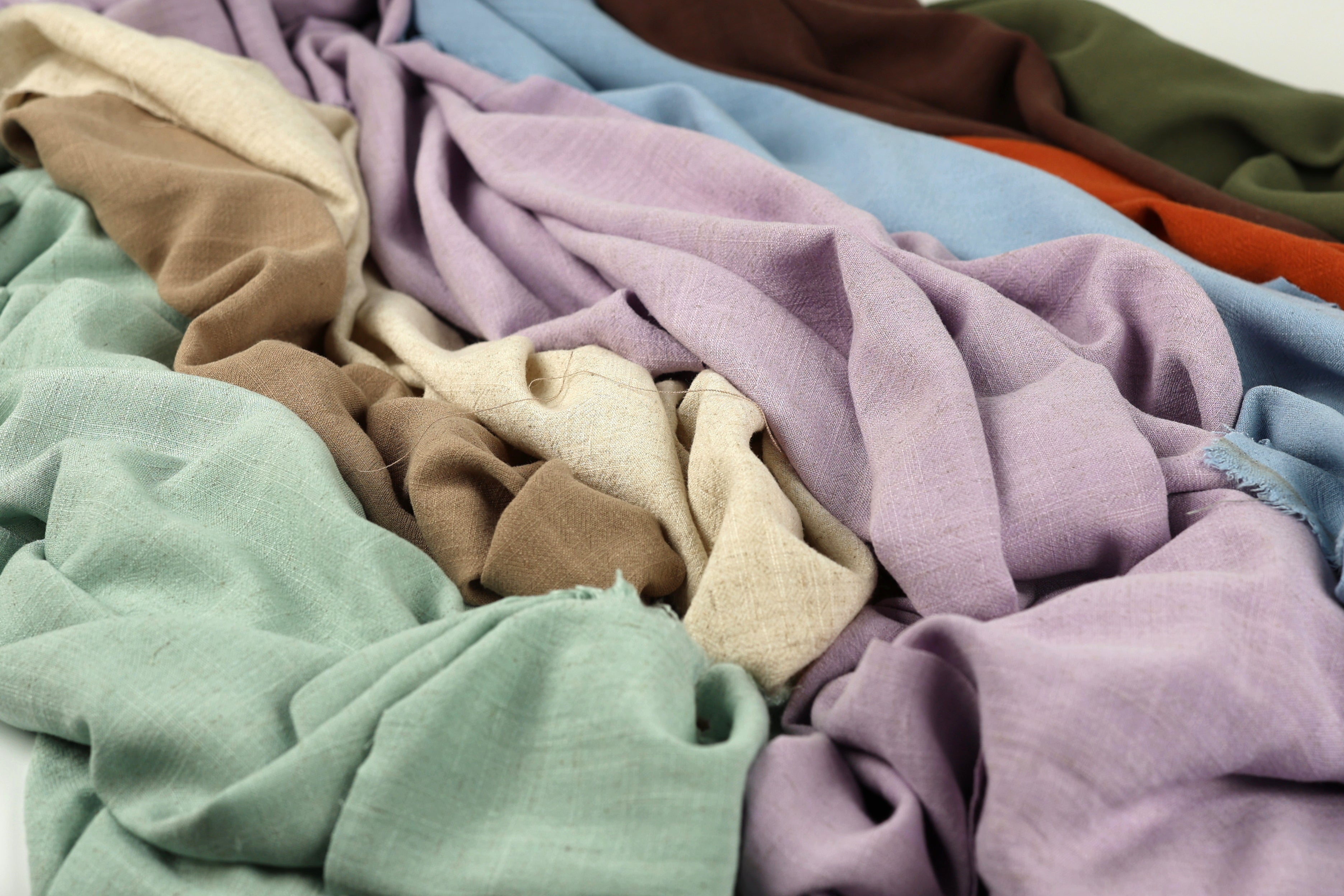 a close-up view of various colorful fabric swatches, including shades of green, purple, and brown, arranged in a messy pile.