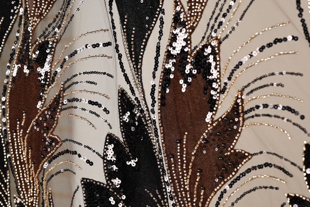 The image is a close-up of a fabric with a floral pattern, featuring a mix of black, brown, and white sequins and beads. The pattern is intricate and detailed, with the sequins and beads arranged in a way that creates a visually striking design.