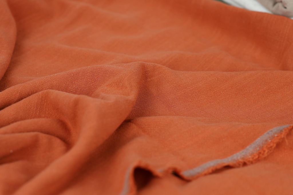 a close-up view of a crumpled orange fabric, with a slight texture and folds visible.