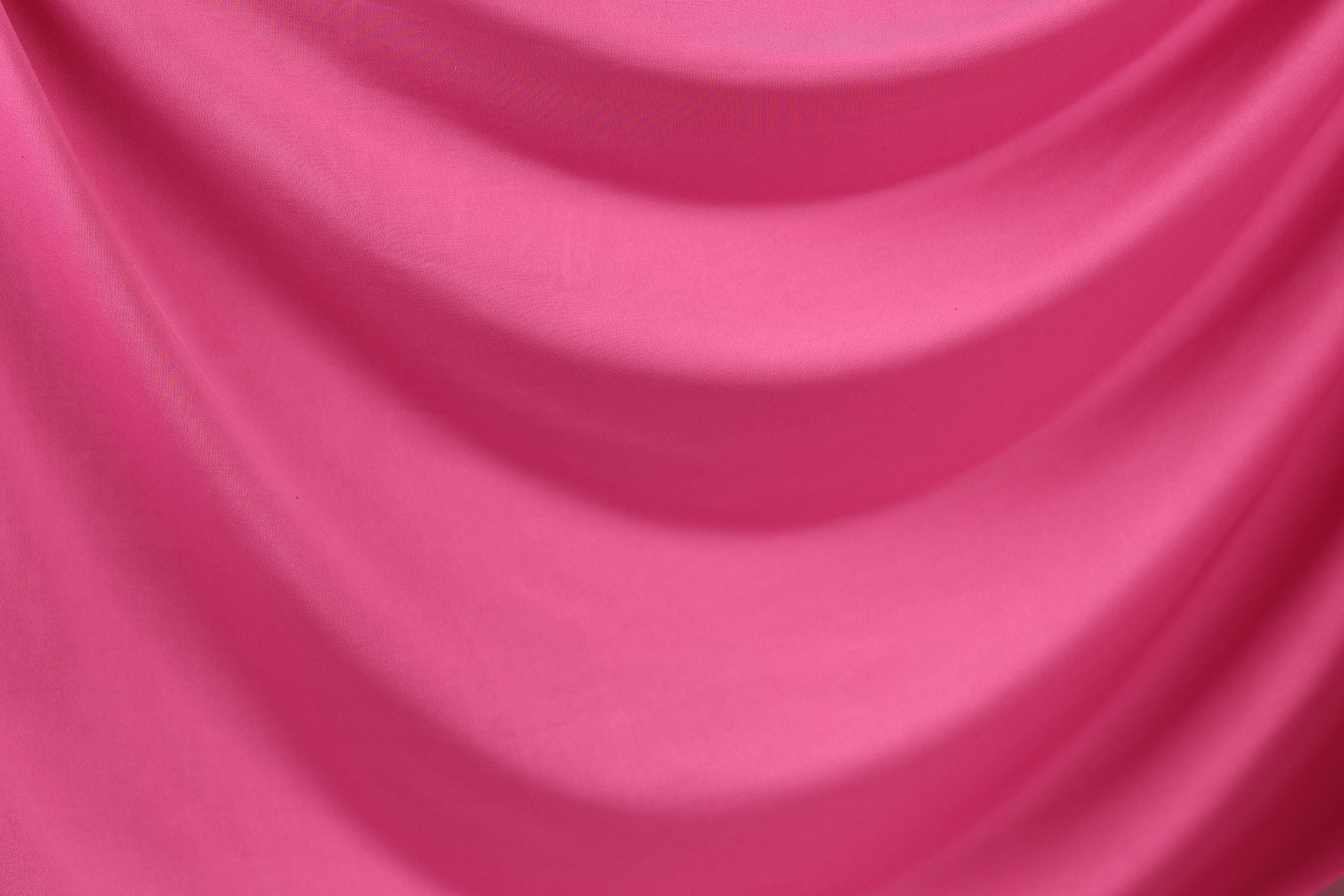 The image is a close-up of a bright pink fabric, possibly a sheer or satin material. The fabric has a smooth, flowing texture and appears to be made of a soft, shiny material.