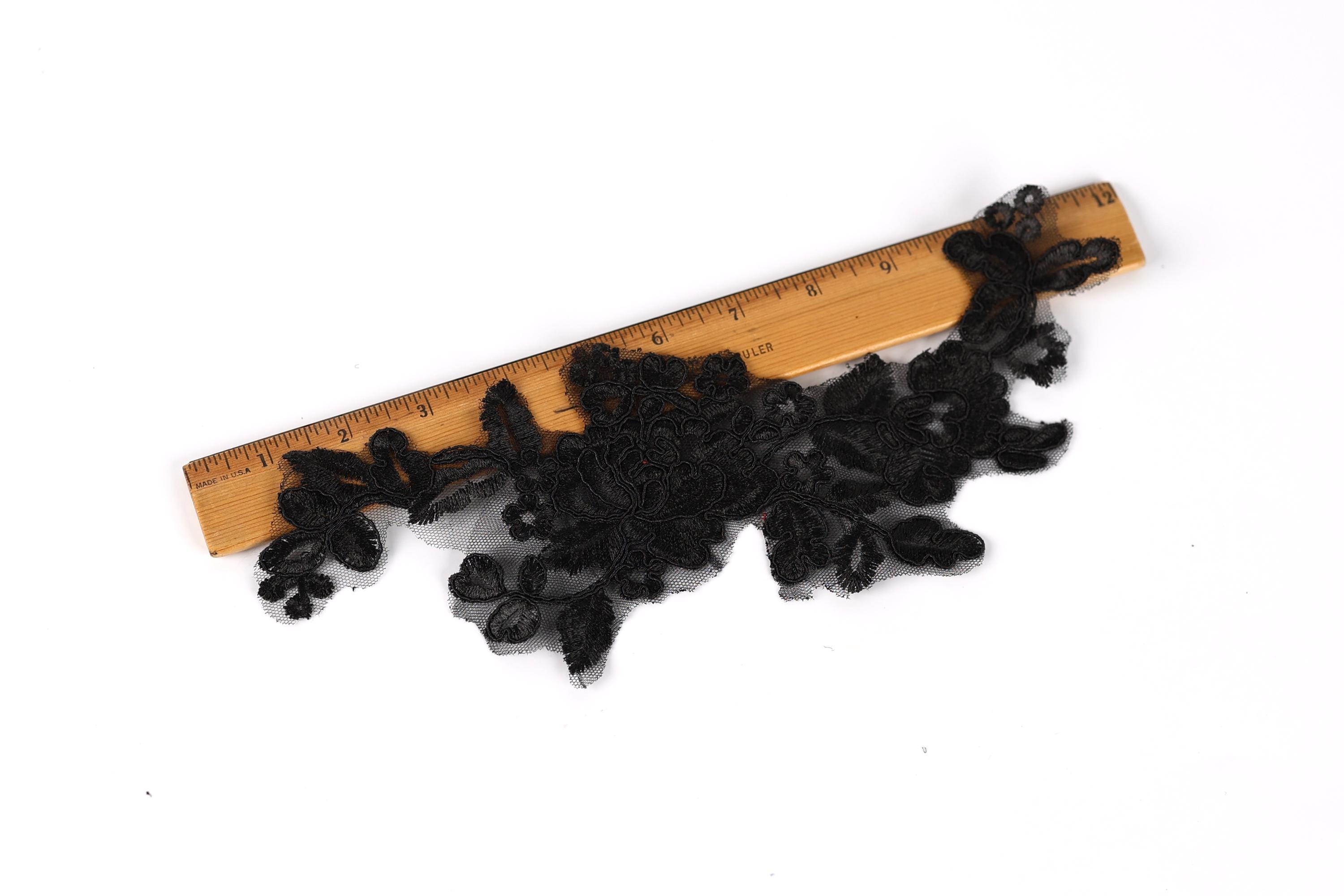 a piece of black lace or thread lying on a wooden ruler, which is placed on a white background.