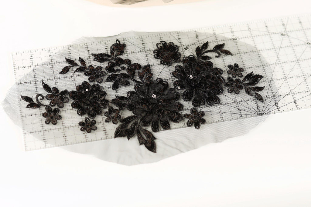a close-up view of a piece of fabric with black embroidered flowers and leaves, placed on a transparent ruler.