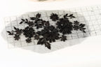 a close-up view of a piece of fabric with black embroidered flowers and leaves, placed on a transparent ruler.