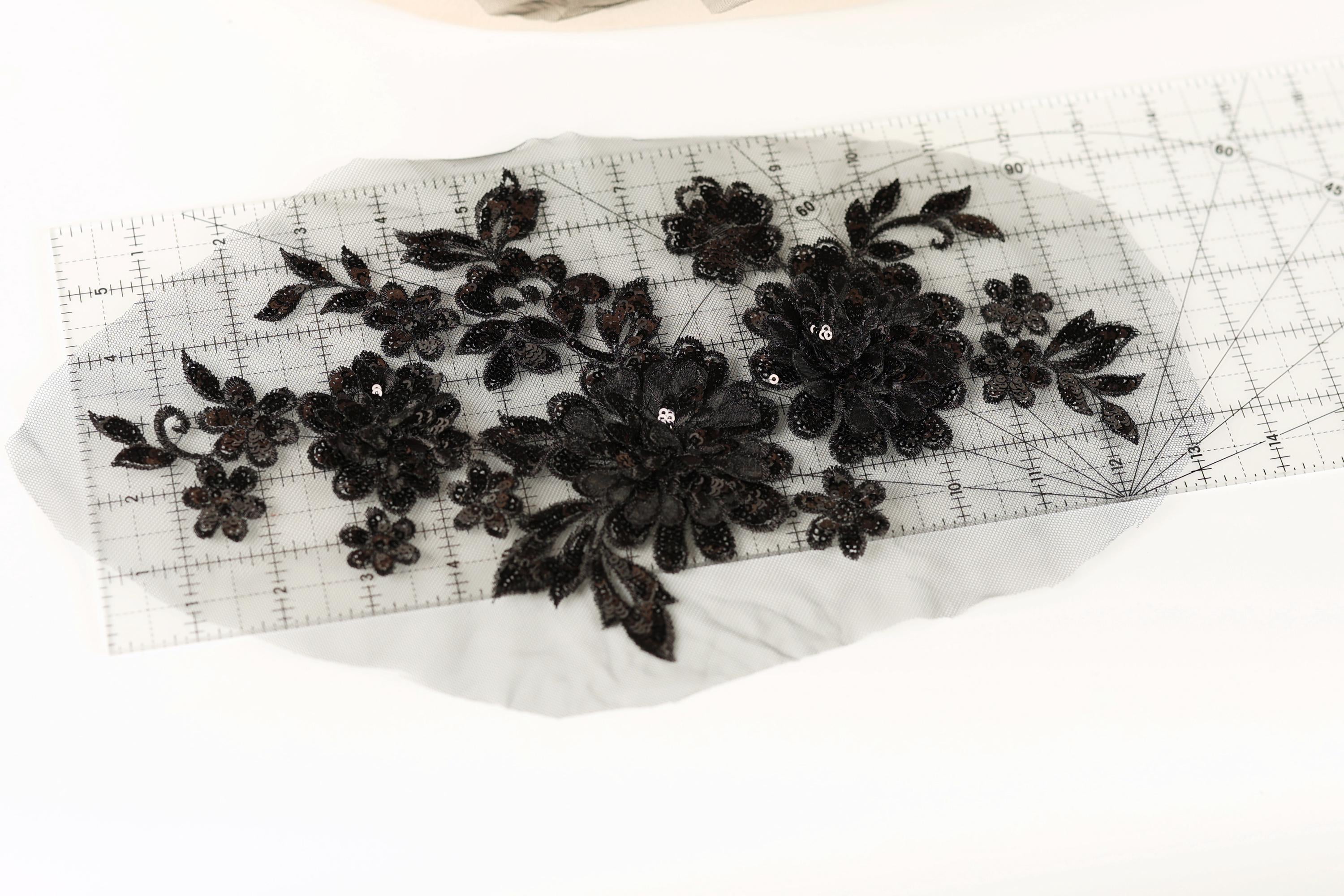a close-up view of a piece of fabric with black embroidered flowers and leaves, placed on a transparent ruler.