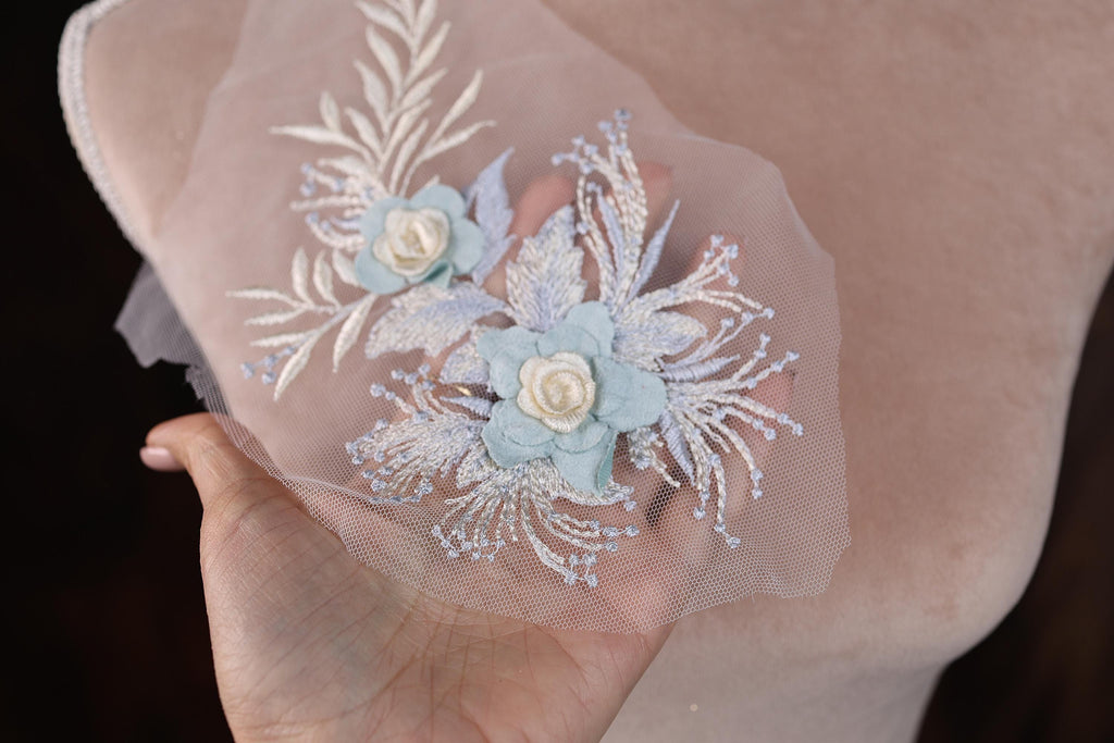 A hand holding a piece of fabric with delicate floral embroidery.