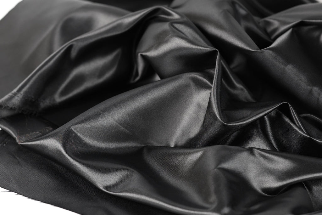 a close-up view of a crumpled, shiny black fabric, possibly silk or satin, with a textured and wrinkled appearance.