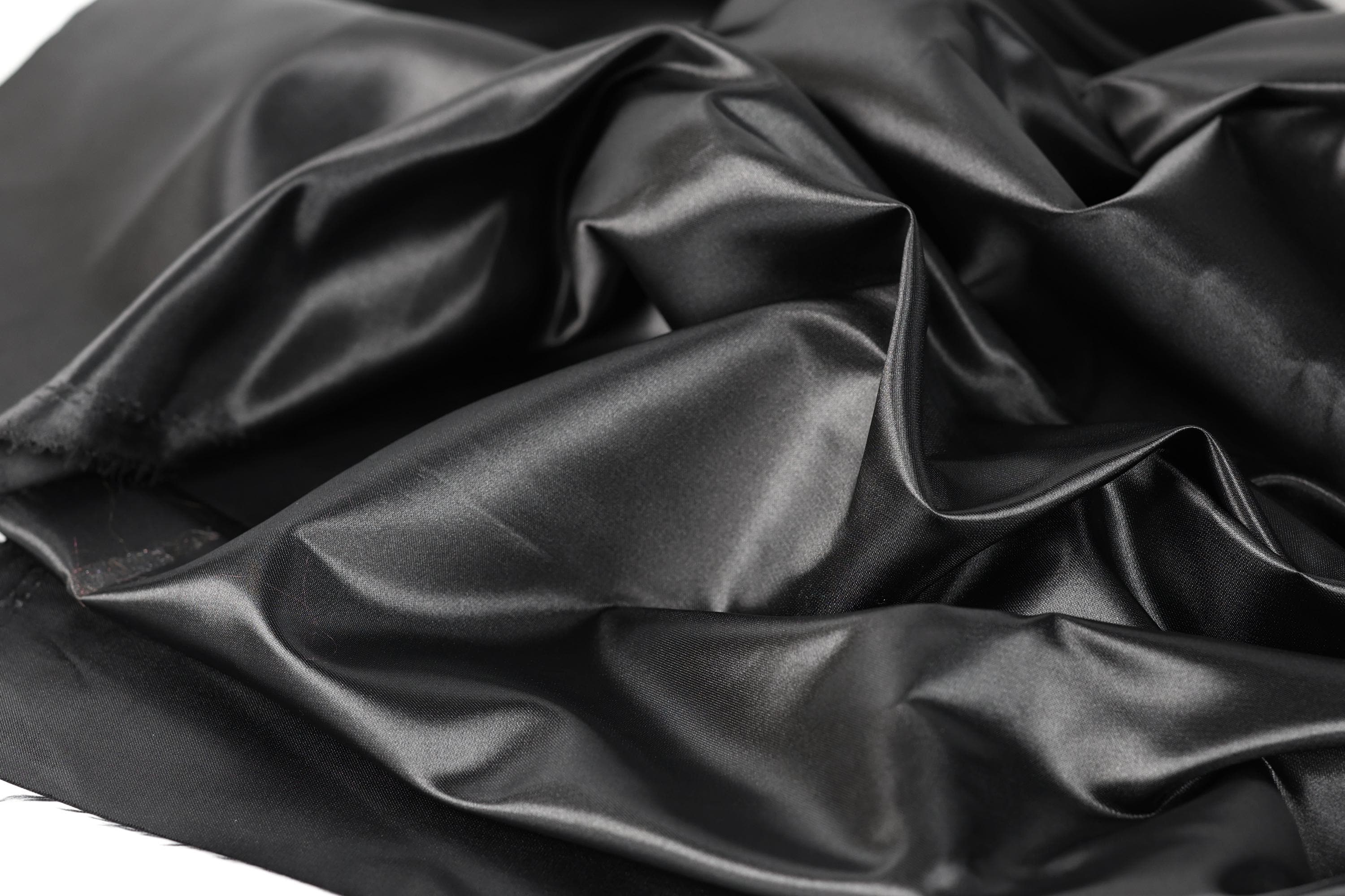 a close-up view of a crumpled, shiny black fabric, possibly silk or satin, with a textured and wrinkled appearance.