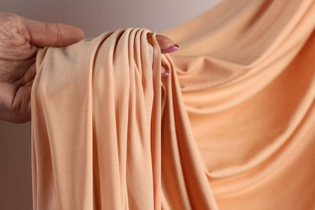A hand is holding a piece of peach-colored fabric, with the fabric partially draped over the hand.