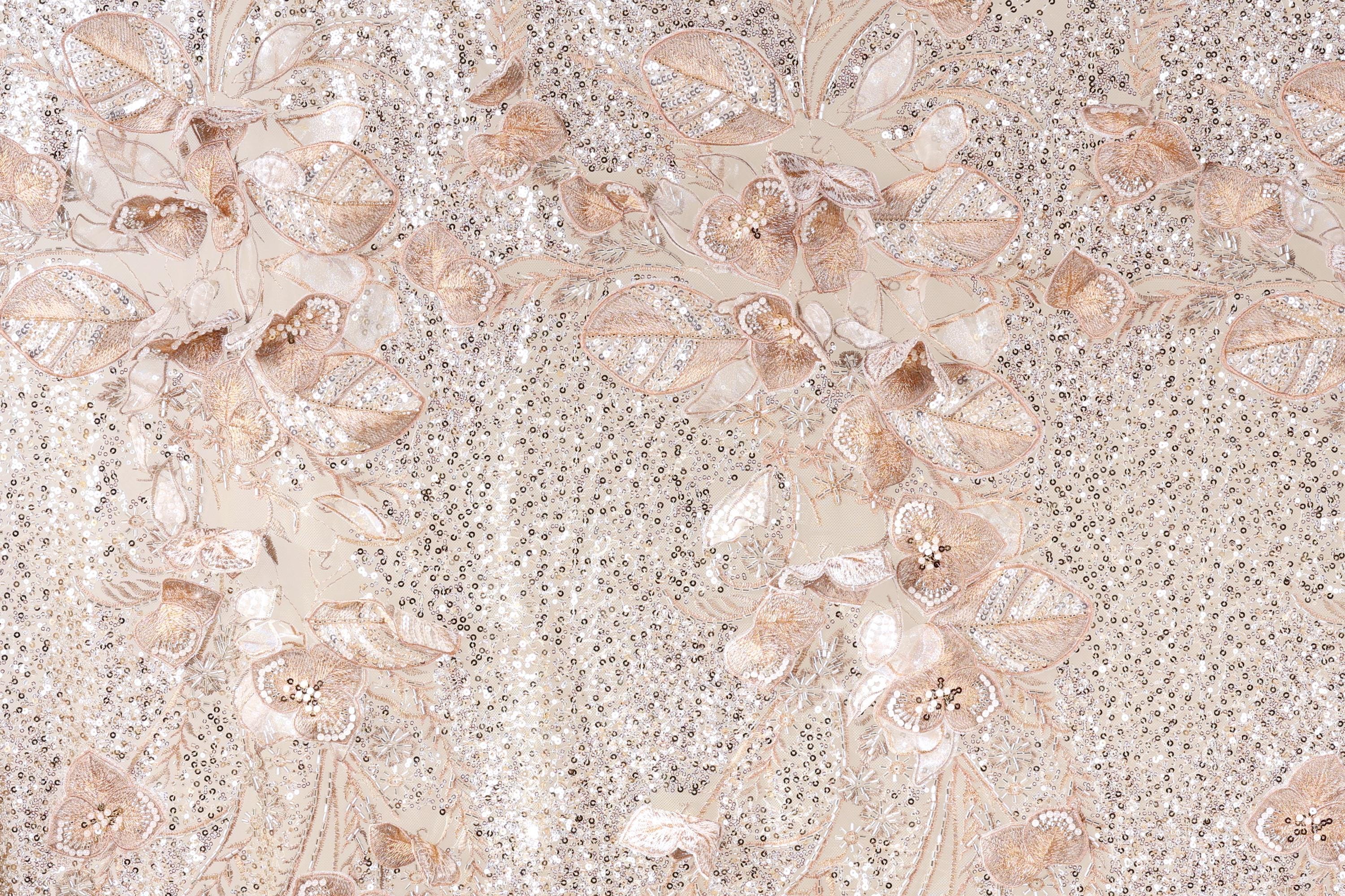 a close-up view of a fabric with a floral pattern, including various shades of pink and white flowers and leaves. The fabric appears to be made of a shiny, sequined material, giving it a sparkling and elegant appearance.
