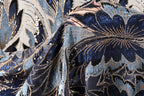 a close-up view of a fabric with a floral pattern, featuring a mix of blue, black, and gold colors. The fabric appears to be made of a shiny material, possibly sequin or beads, and has a textured appearance.