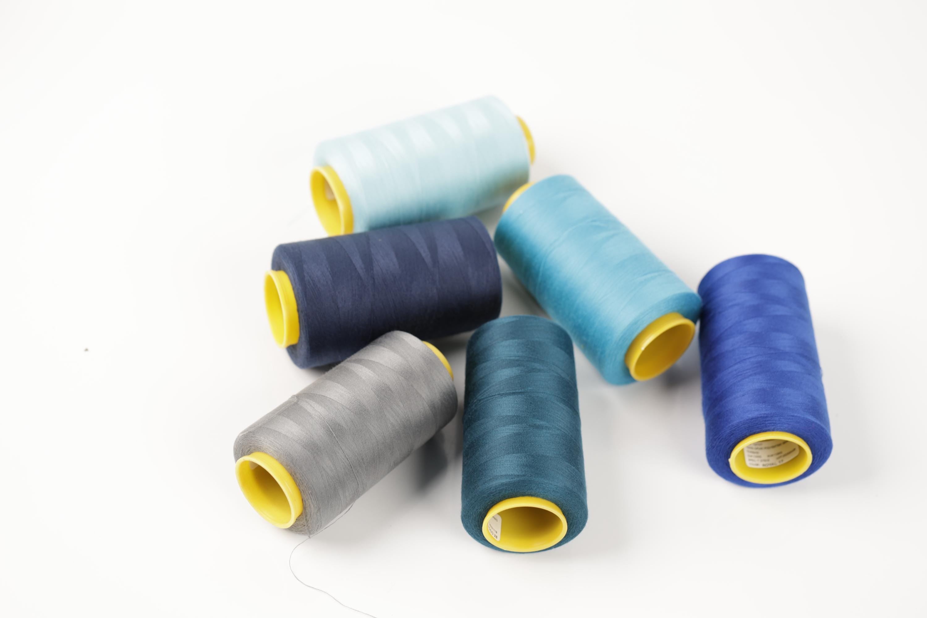 a collection of six spools of thread in various colors, including blue, gray, and yellow, arranged on a white background.
