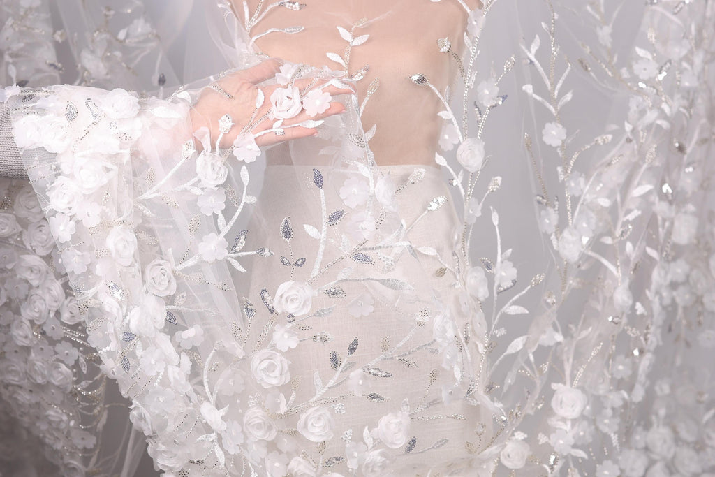 A close-up view of a white wedding dress with intricate floral embroidery, including white roses and leaves.