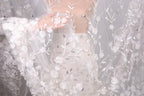 A close-up view of a white wedding dress with intricate floral embroidery, including white roses and leaves.