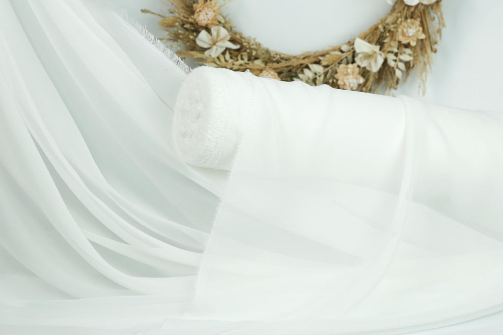 a white fabric, possibly a sheer or sheer curtain, with a wreath of flowers in the background.
