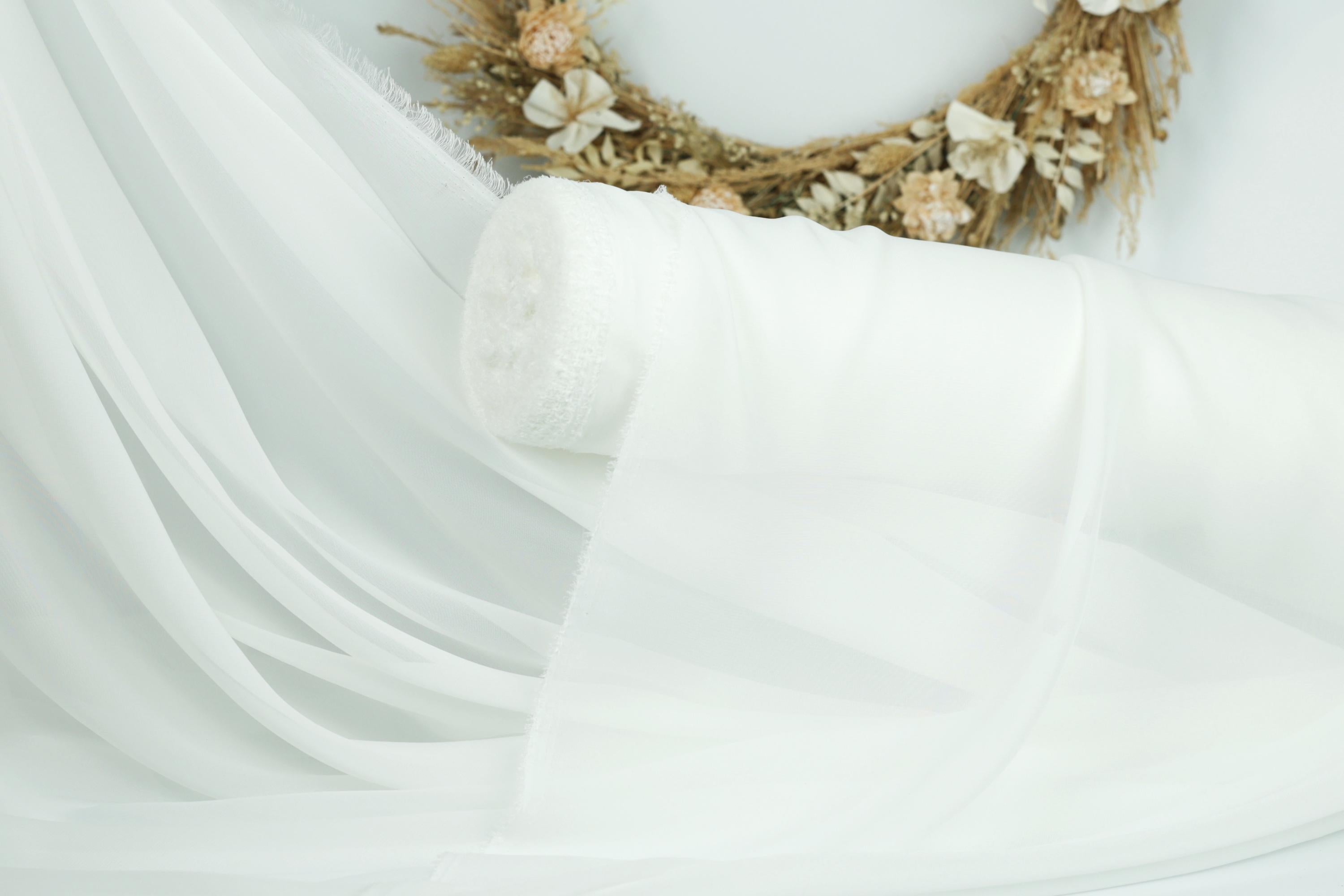 a white fabric, possibly a sheer or sheer curtain, with a wreath of flowers in the background.