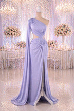 A lavender one-shoulder gown with a long train and a high slit on the side, displayed on a mannequin in a room with a floral backdrop.