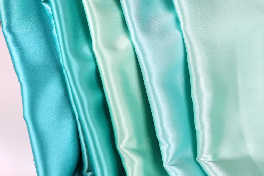 A close-up image of a collection of turquoise-colored satin fabric, with the fabric appearing to be folded or draped in a vertical arrangement.