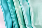 A close-up image of a collection of turquoise-colored satin fabric, with the fabric appearing to be folded or draped in a vertical arrangement.