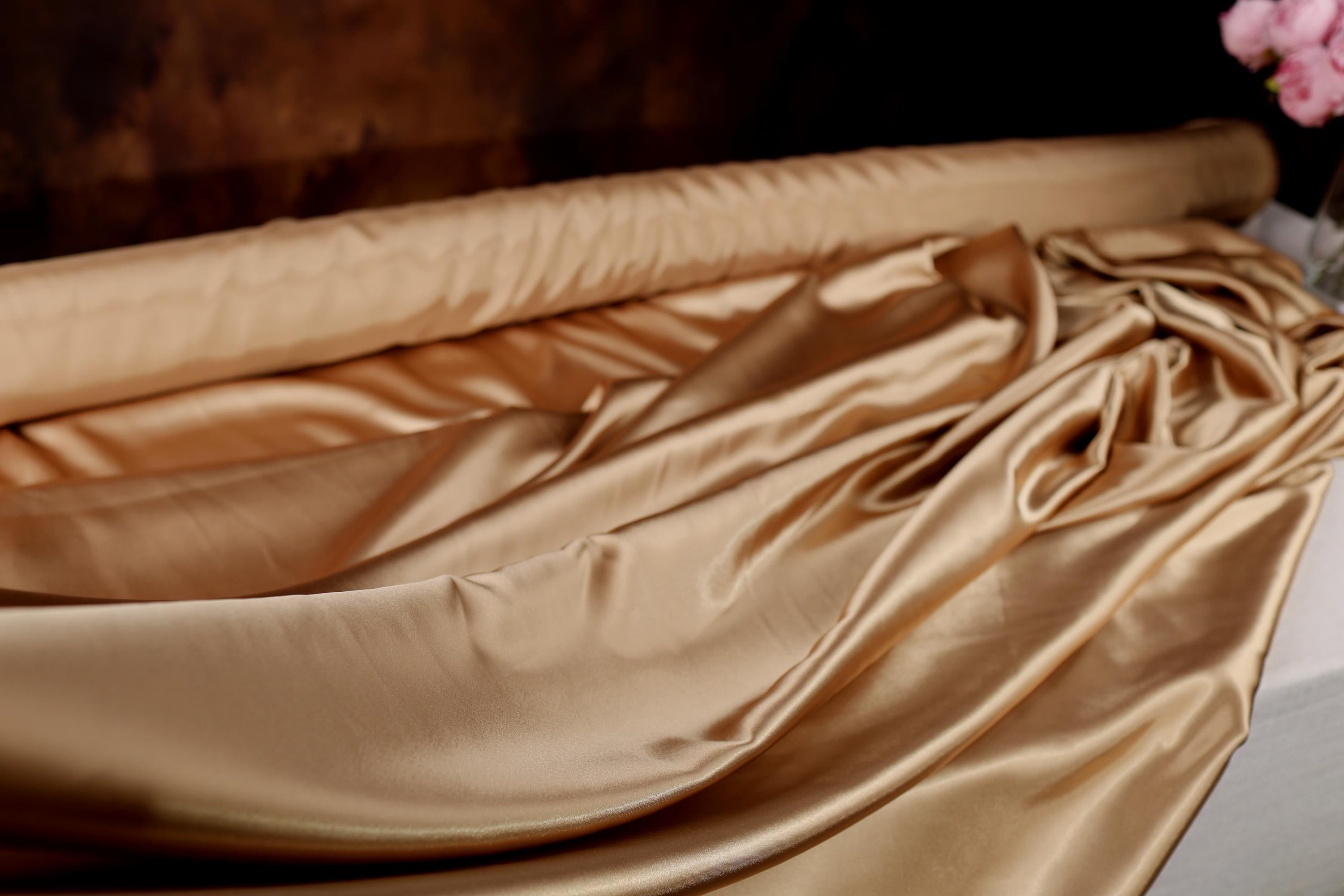 A close-up view of a luxurious, shiny gold fabric, possibly silk or satin, with a smooth, flowing texture.