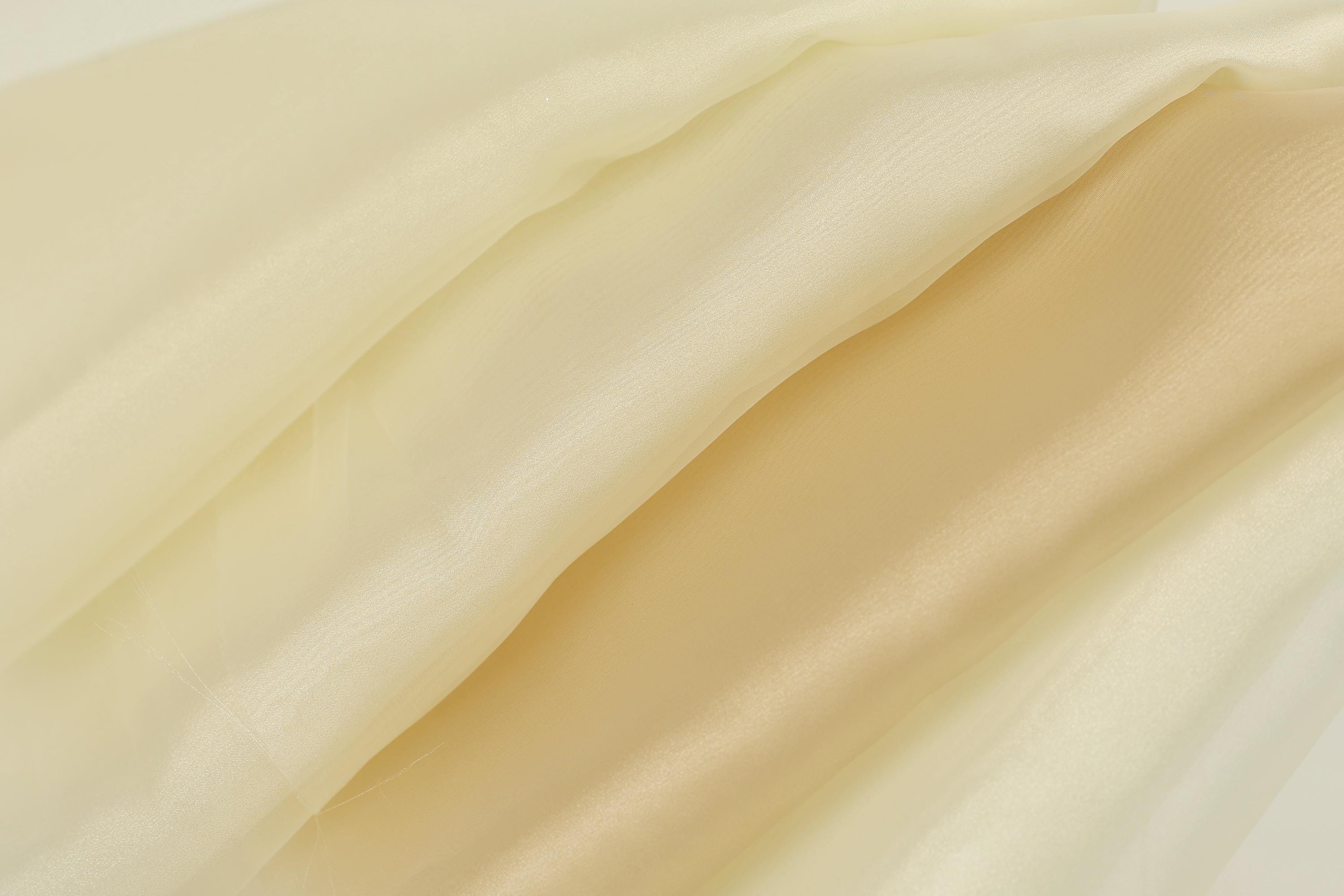 The image is a close-up of a fabric with a soft, flowing texture in shades of yellow and cream.