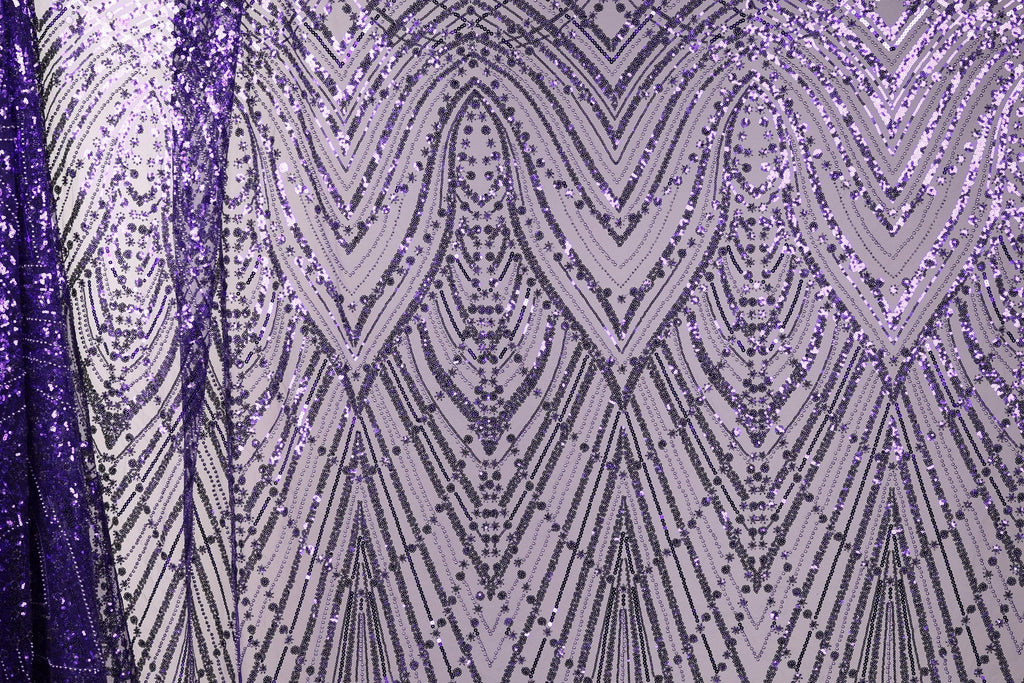 a close-up view of a fabric with a purple and white pattern, consisting of a repeating diamond-shaped motif with a metallic sheen. The pattern is composed of numerous small dots and lines, creating a visually striking and intricate design.