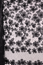 The image is a close-up of a black and white fabric with a floral pattern. The fabric appears to be made of lace or a similar material, with a repeating floral design in black and white. The image does not contain any text or additional objects, and the focus is solely on the intricate floral pattern on the fabric.
