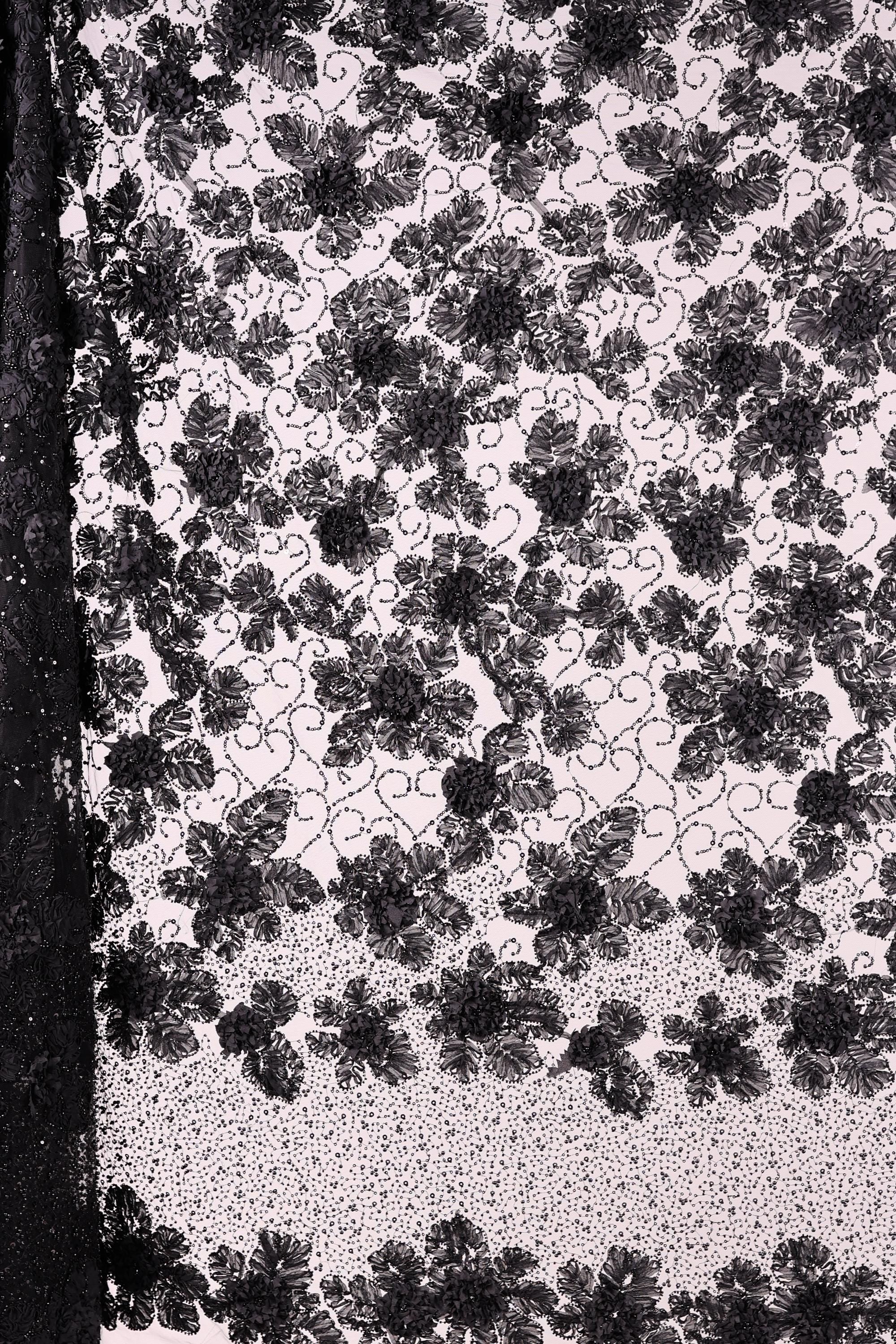 The image is a close-up of a black and white fabric with a floral pattern. The fabric appears to be made of lace or a similar material, with a repeating floral design in black and white. The image does not contain any text or additional objects, and the focus is solely on the intricate floral pattern on the fabric.
