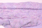 a close-up view of a fabric with a purple floral pattern, featuring small white and silver embellishments.