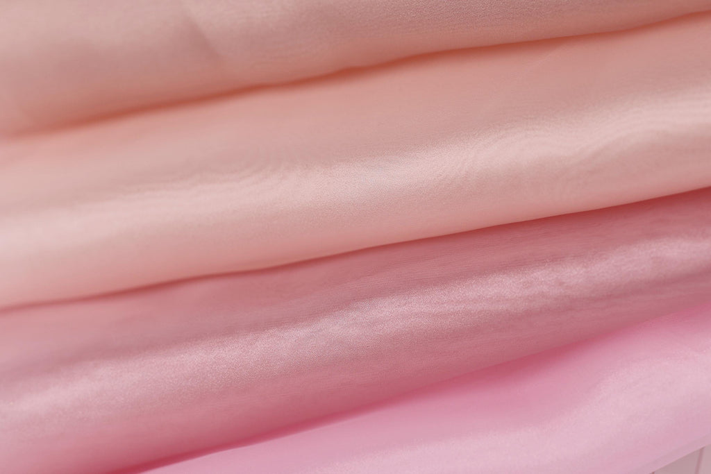 A close-up image of a soft, light pink fabric, with a subtle gradient effect transitioning from a darker shade to a lighter one.