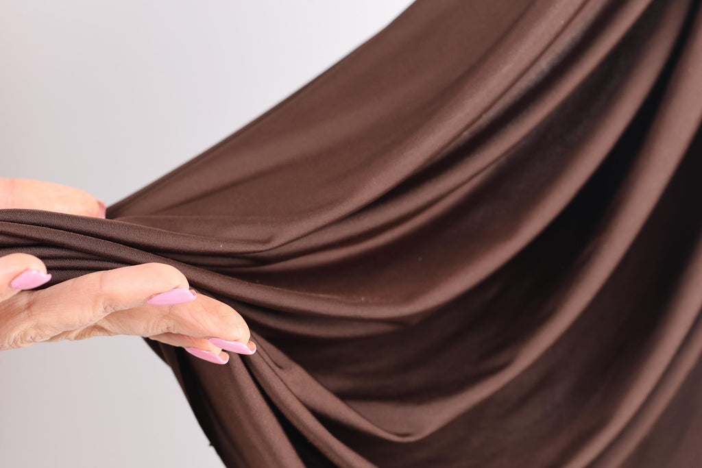 A hand with painted fingernails is holding a brown fabric, which appears to be a piece of clothing or a textile.