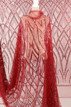 a mannequin wearing a red sequin dress with a sheer overlay. The dress has a long, flowing cape-like design with a red and white pattern. The background is a pink and white patterned fabric.