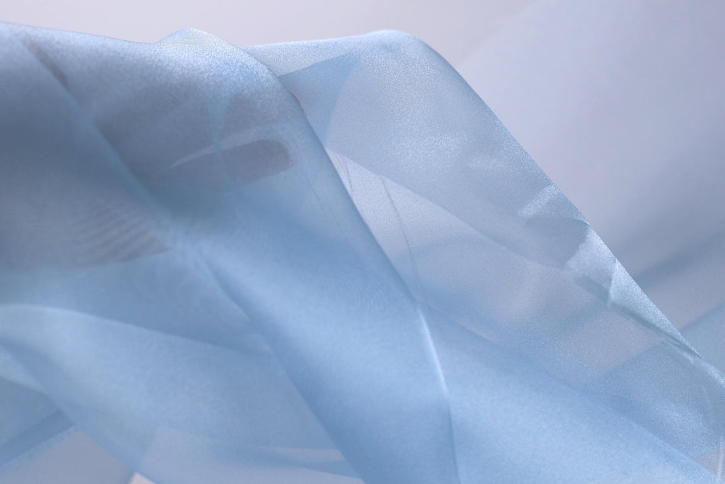 The image is a close-up of a light blue fabric, possibly silk or chiffon, with a soft, flowing texture.