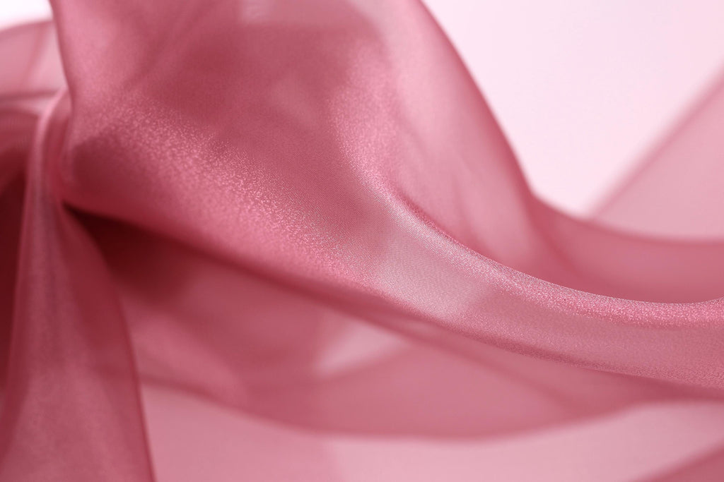 A close-up view of a soft, flowing pink fabric, possibly silk or chiffon, with a smooth and shiny texture.