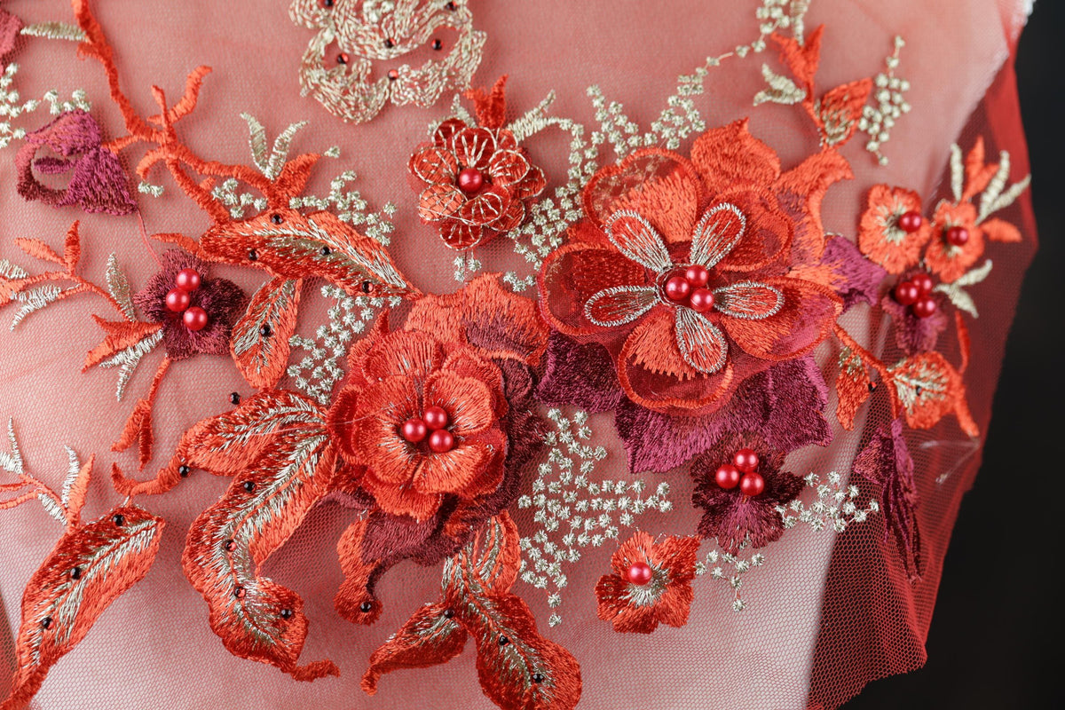 a close-up view of a delicate, intricately embroidered fabric with a floral design. The fabric is adorned with a variety of red flowers and leaves, as well as small red berries, creating a vibrant and eye-catching pattern. The embroidery work is detailed and precise, showcasing the skill and craftsmanship involved in creating this beautiful textile art piece.