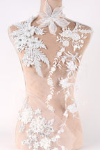 A mannequin wearing a white dress with intricate floral embroidery and lace details.