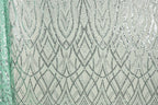 a close-up view of a fabric with a repeating pattern of silver and green sequin designs. The pattern consists of a series of diamond shapes and lines, creating a visually striking and intricate design. The fabric appears to be a light green color, which complements the silver and green sequins. The image does not contain any text or other discernible objects, and the focus is solely on the detailed pattern of the sequin design.