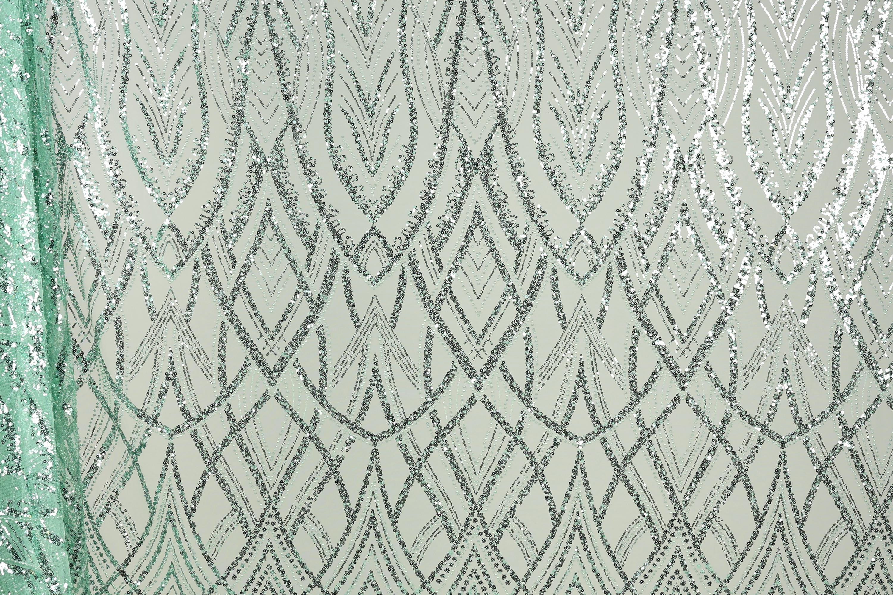a close-up view of a fabric with a repeating pattern of silver and green sequin designs. The pattern consists of a series of diamond shapes and lines, creating a visually striking and intricate design. The fabric appears to be a light green color, which complements the silver and green sequins. The image does not contain any text or other discernible objects, and the focus is solely on the detailed pattern of the sequin design.