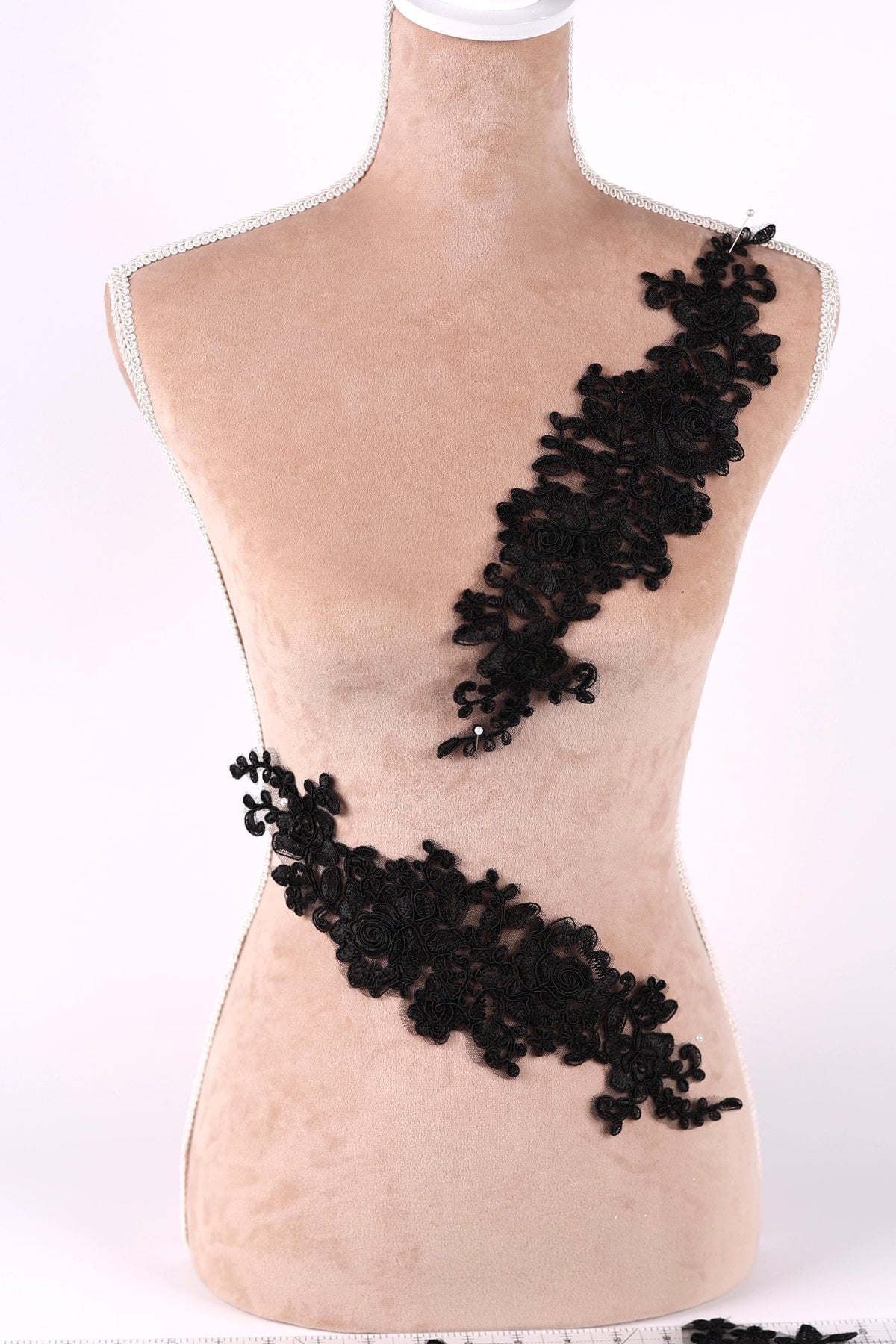 A mannequin torso with black lace or floral embroidery attached to it.
