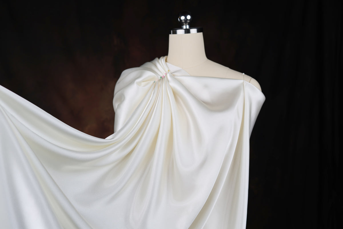 A mannequin wearing a white satin dress with a draped, flowing skirt.