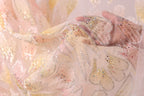 A close-up view of a delicate, hand-embroidered fabric with a floral pattern. The fabric appears to be made of sheer material, with a light pink and white color scheme. The intricate embroidery and beading on the fabric create a visually appealing and delicate appearance.